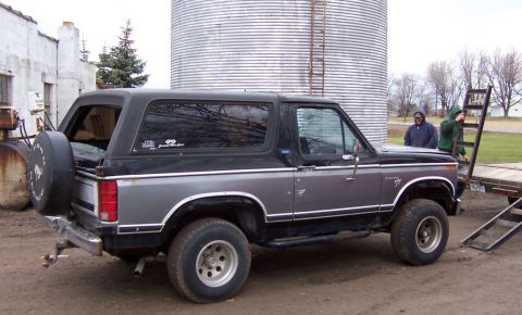 1978 Ford Bronco - A two-tone Ford Bronco is parked outdoors near a large metal silo and some industrial equipment.