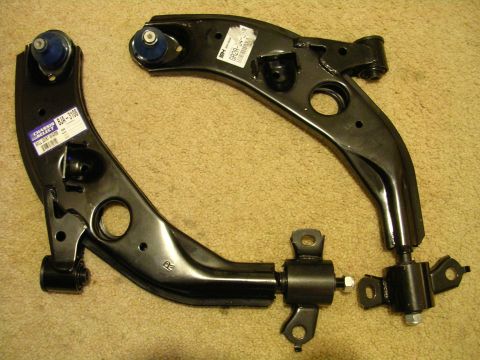 1996 Ford Probe - Two new car control arms are laid out on a carpeted surface, ready for installation.