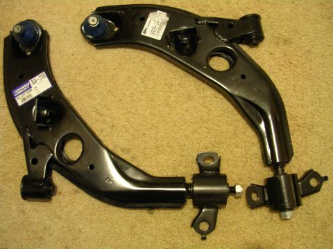 1996 Ford Probe - Two black lower control arms with blue ball joints and labels are shown on a carpeted surface.