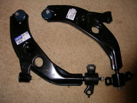 1996 Ford Probe - Two black lower control arms are displayed, one with a blue bushing and a label reading BJA-3106, the other with a label reading GP29-04-19.