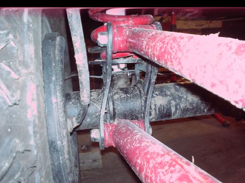 1984 Ford Bronco - Close-up view of the rear suspension and tire, showing red-painted components covered in mud.