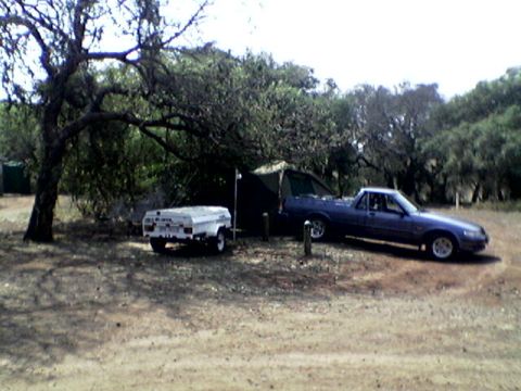1973 Ford Ranchero - A blue pickup truck and a small white trailer are parked in a wooded area next to a tent.