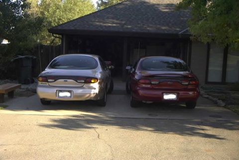 1999 Ford Taurus - Two sedans, a silver one and a red one, are parked side-by-side in front of a garage.