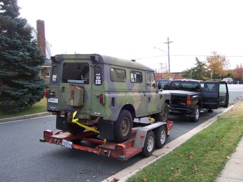 1974 Land Rover Land Rover - A camouflaged 1974 Land Rover Land Rover is loaded onto a trailer behind a pickup truck.