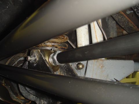 1996 Ford Bronco - Tight underside shot of a suspension mount where black tube bars cross over a bracket secured by a large hex nut and washer, with a white/s…