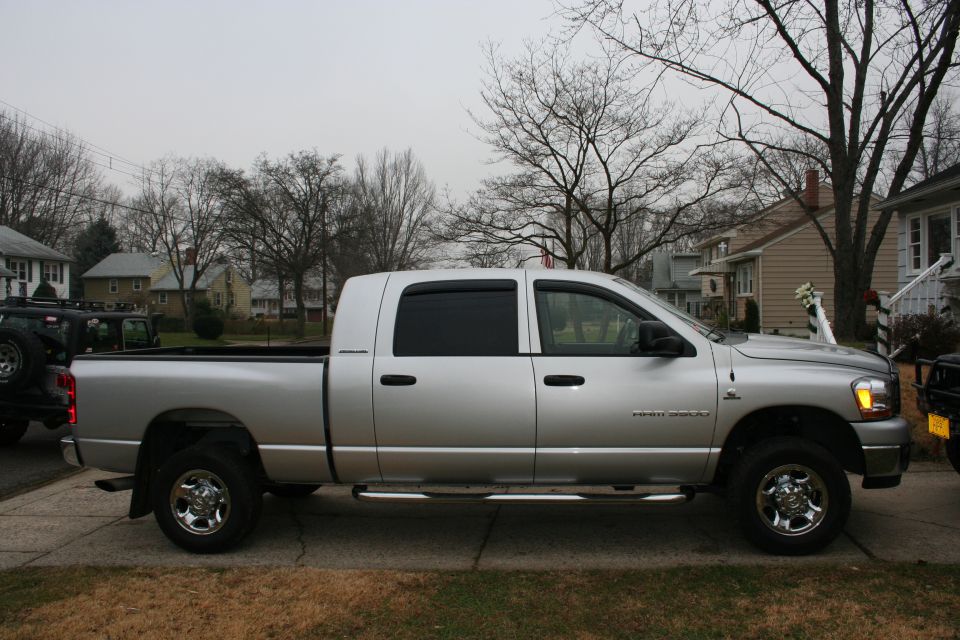 Silver 2006 Dodge 3500 pickup truck parked on a residential street, with a black Jeep visible to the left