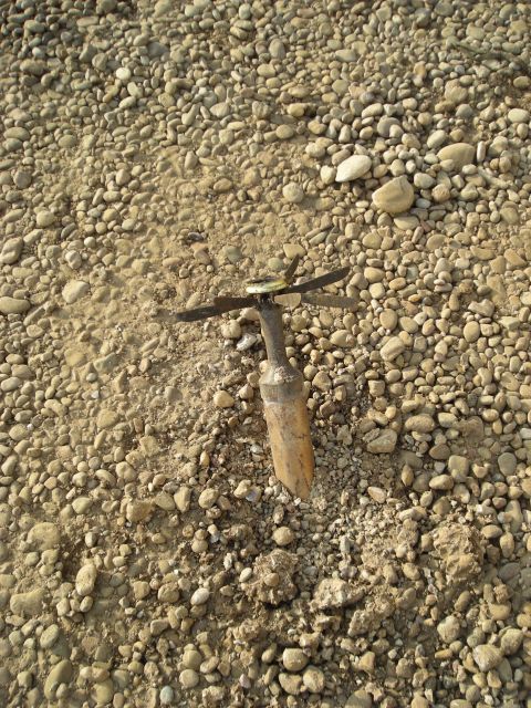 1996 Ford Probe - A stake with propeller-like blades is partially embedded in a surface covered with small stones and dirt.