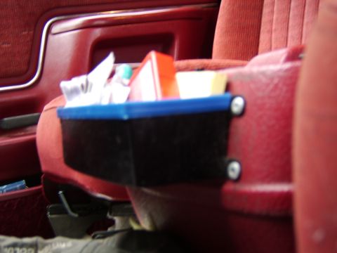1989 Ford Bronco - A black organizer with a blue trim is attached to the red seat of a vehicle, holding various items.