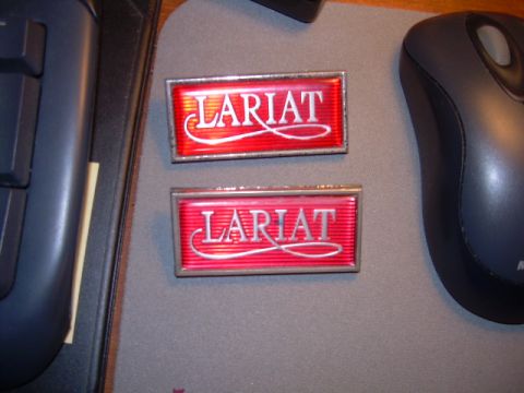 1984 Ford Bronco - Two red emblems with the word Lariat are shown on a desk next to computer peripherals.