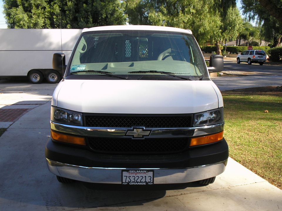White Chevrolet Express van front view on a driveway with California plate and tow mirrors