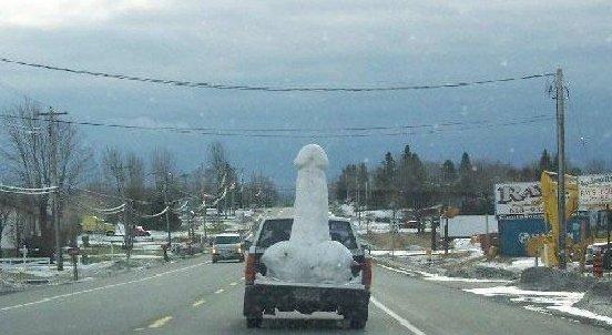 Pickup truck with a large snow sculpture in its bed, driving on a snowy road