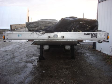 2006 Ford F-350 - A flatbed trailer is loaded with rolled up tarps and other materials, parked on a wet surface.