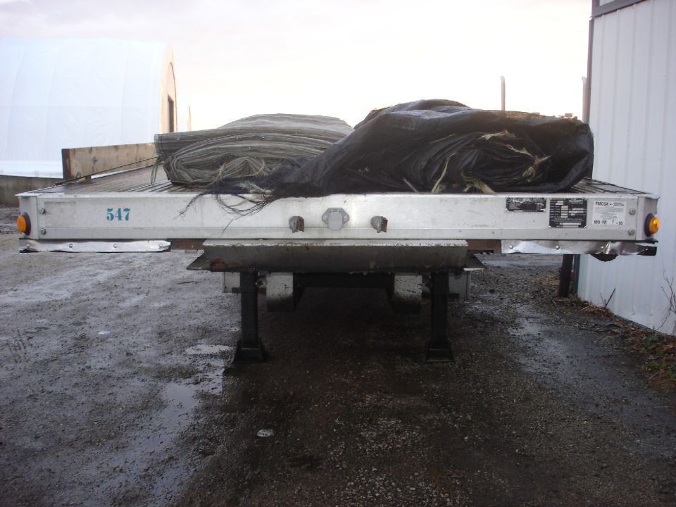 Flatbed trailer with tarped cargo, showing number 547 on the side