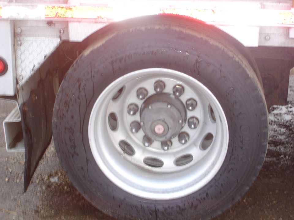 Truck wheel with chrome lug nuts and a black tire, next to a white fender and mud flap