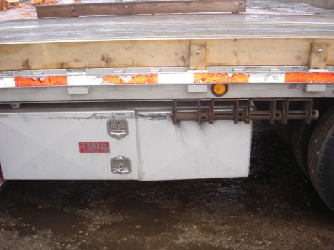 2006 Ford F-350 - Toolbox with TMI logo on a flatbed trailer, showing part of a tire and trailer bed.