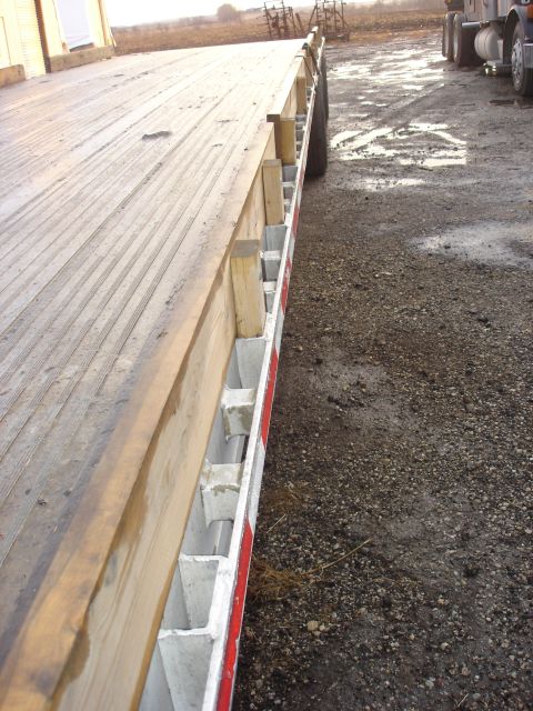 2006 Ford F-350 - A flatbed trailer is shown from the side, with a truck visible in the background on a gravel lot.