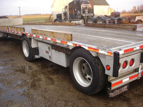2006 Ford F-350 - A flatbed trailer is parked on a muddy lot next to a semi-truck cab.