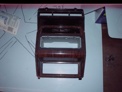 1984 Ford Bronco - This is a dashboard trim piece with a woodgrain finish and an 'XLT' emblem, likely for a car stereo installation.