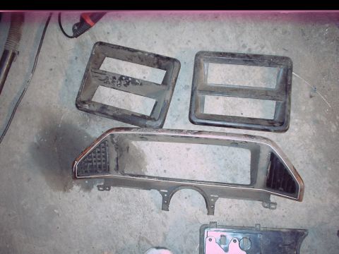 1984 Ford Bronco - Three automotive parts, likely headlight bezels and a grille surround, lie on a concrete surface. A Supermotors.net logo is visible at the…