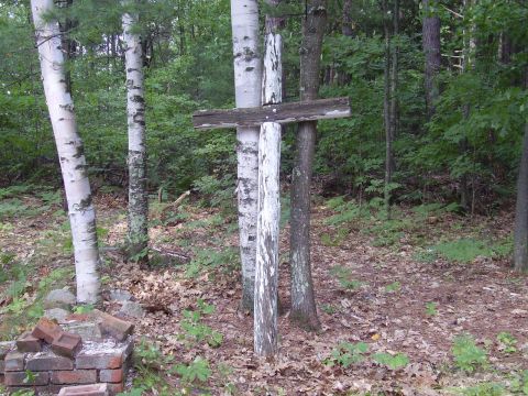 1996 Ford F-150 - A weathered wooden cross stands among trees in a wooded area, with a pile of bricks nearby.