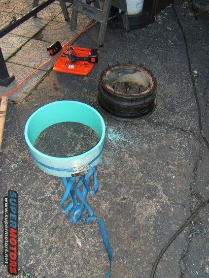 1980 Jeep CJ5 - Automotive parts, including a blue pipe and a metal rim, are laid out on asphalt near a power tool.