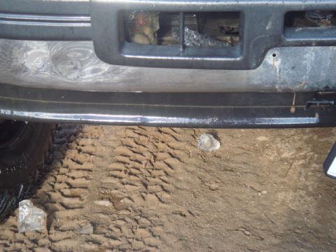 1996 Ford Bronco - Close-up of a vehicle's front end, showing the bumper and grille area with tire tracks in the muddy ground.