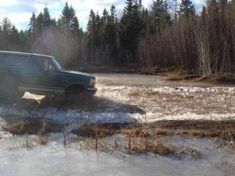 1996 Ford Bronco - A 1996 Ford Bronco navigates a challenging icy and muddy terrain, kicking up water and slush.