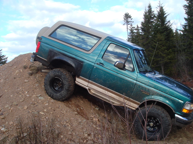 Green Ford Bronco climbing a dirt hill with trees in the background