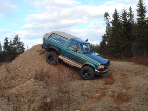1996 Ford Bronco - A green 1996 Ford Bronco navigates an off-road trail on a cloudy day.