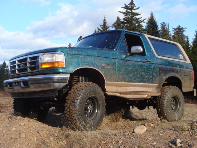 Green lifted 1996 Ford Bronco parked on dirt with trees in background