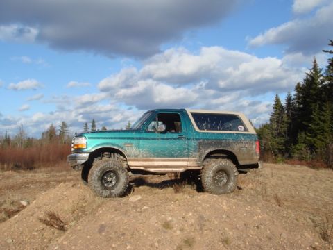 1996 Ford Bronco - This lifted 1996 Ford Bronco is shown off-roading on a dirt hill under a cloudy sky.