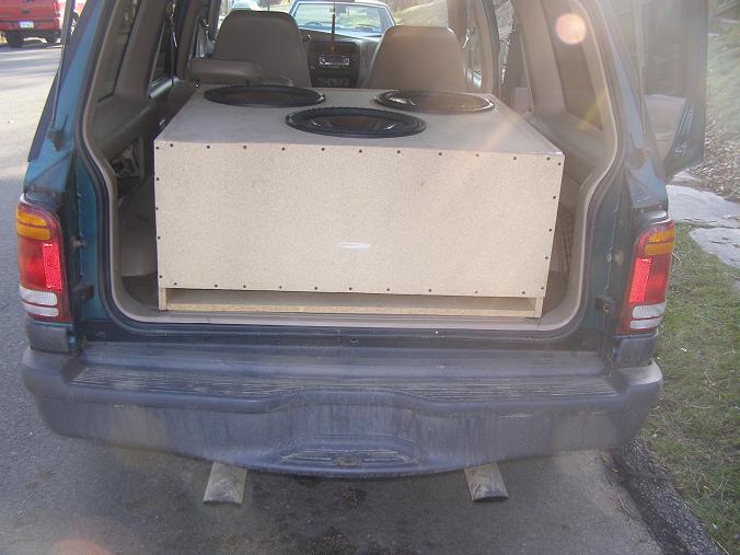MDF triple-sub speaker box in the cargo area of a green SUV with rear liftgate open