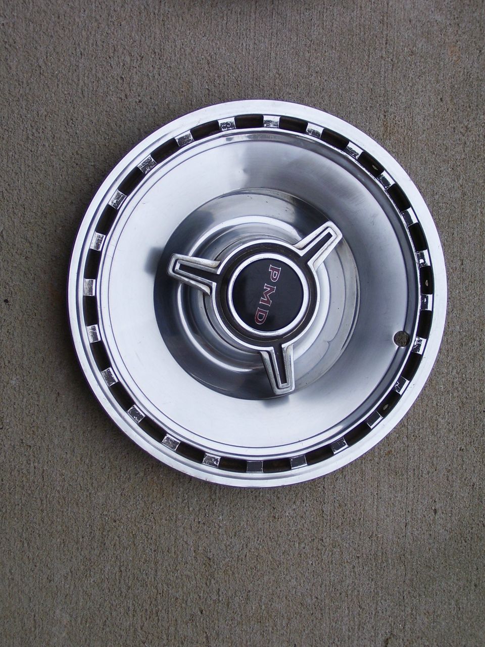 Vintage chrome PMD spinner hubcap lying on a concrete surface