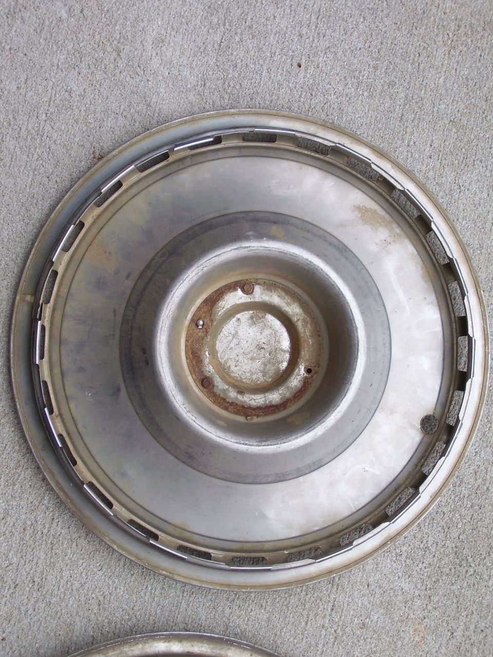 Weathered chrome hubcap face-up on concrete with rusted center