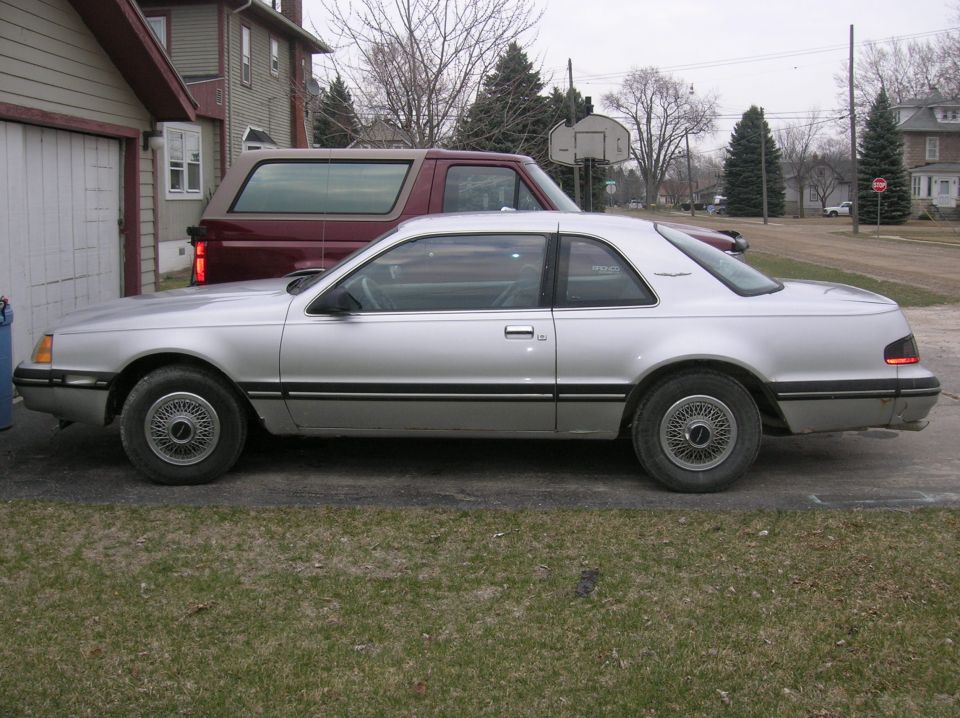 Silver coupe parked next to a red SUV, side view, showing a two-door body style with a black pinstripe
