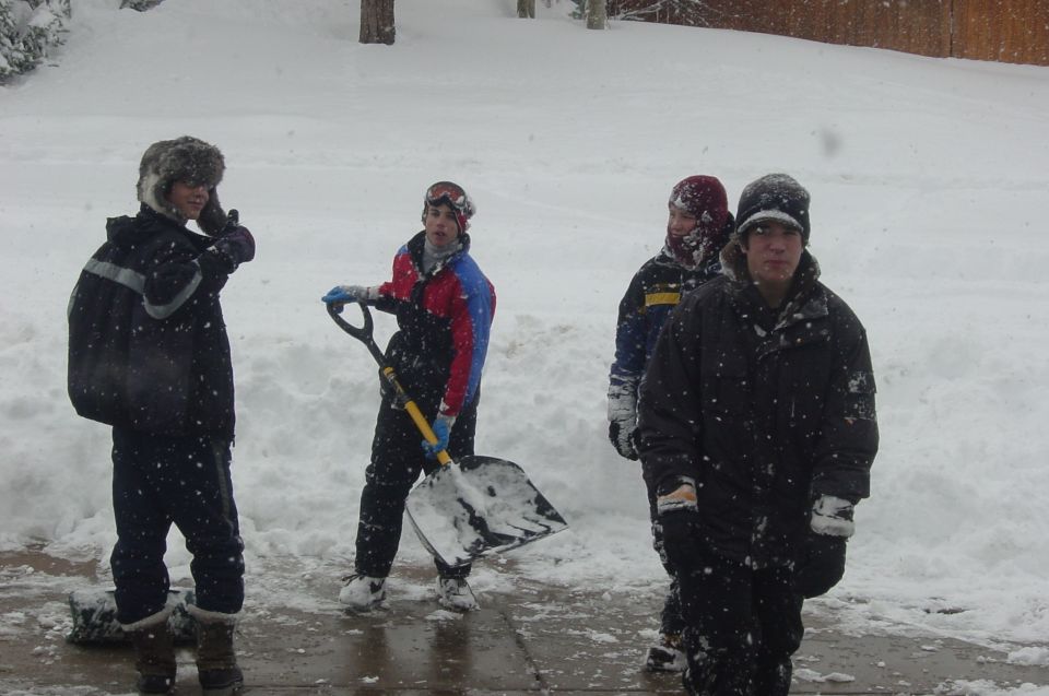 Four people in winter clothing shoveling snow during a snowfall