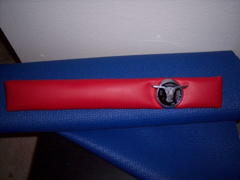 1972 Ford Ranchero - A red trim piece with a chrome bull emblem is shown against a blue textured surface.