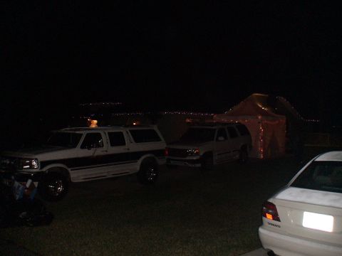 1993 Ford C-350 (Centurion Conversions) - Two SUVs and a tent are visible at night, with a distant city skyline in the background.