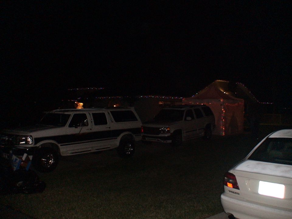 White Ford Bronco SUV with wood paneling parked at night next to another SUV and a tent