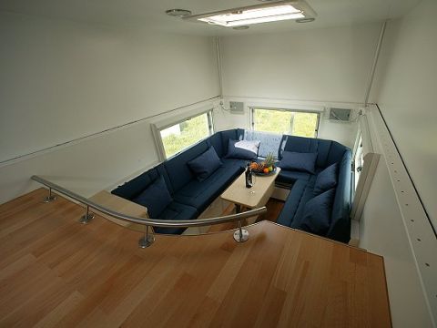 1993 Ford Bronco - The interior of a camper van features a large U-shaped blue sofa, a table with fruit, and wooden flooring.