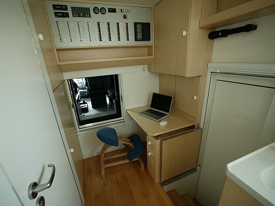 Interior of a camper van with a desk, laptop, and control panel