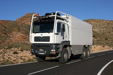 1993 Ford Bronco - A large white expedition truck with off-road tires travels down a highway in a barren, mountainous region under a clear blue sky.
