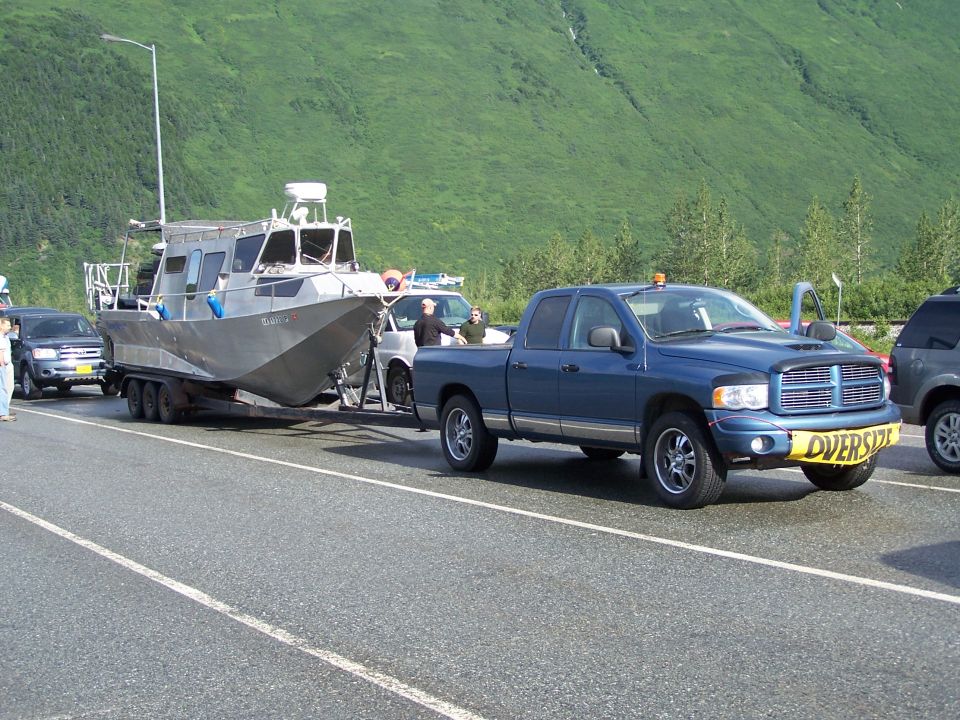 Blue pickup truck towing a boat on a trailer, with an "OVERSIZE" sign on the front bumper
