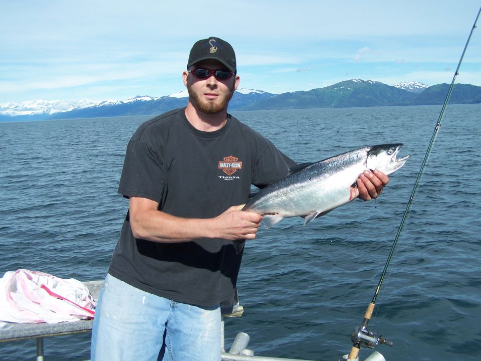 Man holding a large salmon while fishing from a boat with mountains in the background