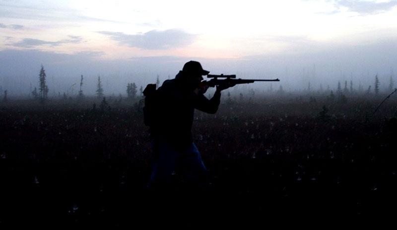 Hunter aiming rifle in foggy field at dawn
