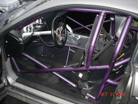 1990 Ford Mustang - Interior view of a modified car a prominent purple roll cage and racing bucket seats.