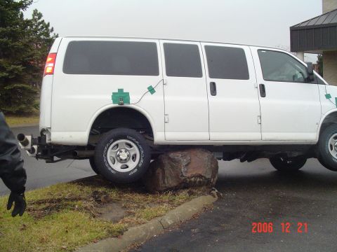 1992 Ford Bronco - A white van is shown with its rear wheel resting on a large rock, with green boxes attached to its exterior.