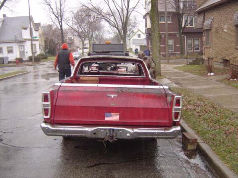 1973 Ford Ranchero - A red pickup truck is parked on a wet street in a residential area.