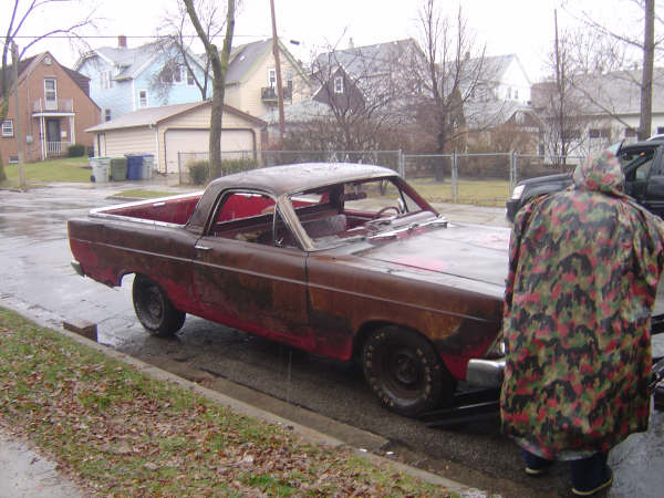 Rusty 1967 Ford Ranchero parked on a wet street, seen from the front passenger side