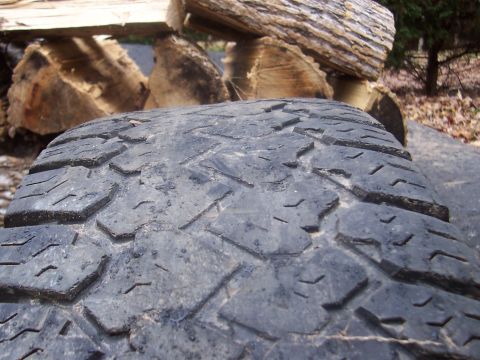 1994 Jeep YJ - A close-up view of a tire tread, with stacked logs and foliage visible in the background.